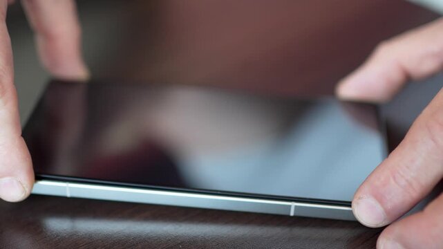 Man hands installing new protective tempered glass on smartphone screen close up.