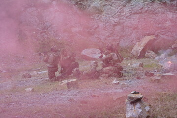 Fototapeta premium multinational group of male soldiers in infantry uniforms, carrying paintball guns and ready for combat, were seen running and practicing military drills, with pink smoke signals being sent 