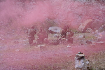 Fototapeta premium multinational group of male soldiers in infantry uniforms, carrying paintball guns and ready for combat, were seen running and practicing military drills, with pink smoke signals being sent 