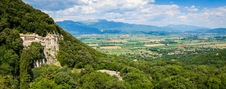 Greccio Lazio Italy 12000px drone panorama of cliffside monastery in rock with scenic mountains green fields background copy space. Authentic Borghi piu belli d Italia hidden gems High Resolution.
