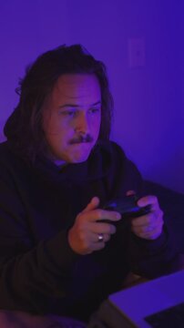 Male gamer playing with controller in purple neon room