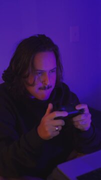 Young Male Gamer Enjoying Console Gaming in Neon-Lit Room