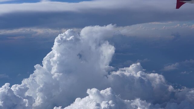 An airplane wing is prominently displayed against a clear blue sky, soaring high above vast formations of fluffy white cumulus clouds during daytime travel