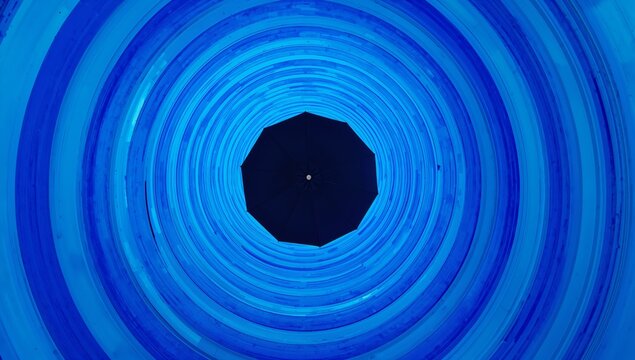 Black umbrella viewed from below inside a circular blue tunnel with concentric rings, creating a striking visual contrast and depth perception