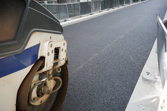 Road roller steel drum pressing fresh dark tarmac