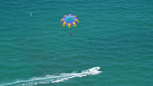 A vibrant, multicolored parasail carries a person high above the clear blue ocean