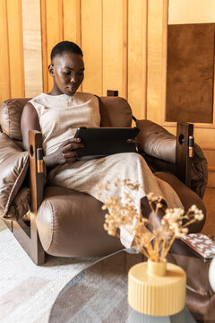 Woman Sits on Brown Chair and Uses Tablet in Modern Indoor Space
