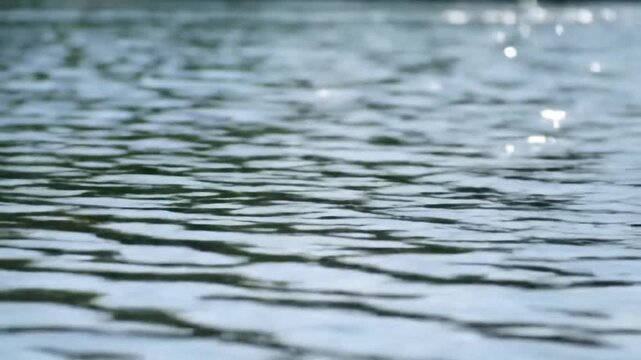 Close-up view of continuous small ripples and wave patterns on a dark blue water surface with soft sunlight reflections and a shallow depth of field bokeh background.