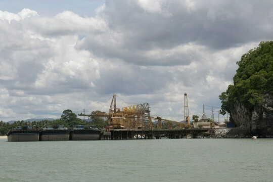 industrial belt conveyor terminal facility loading bulk mineral materials onto large cargo barge transport vessels moored at khanom shoreline