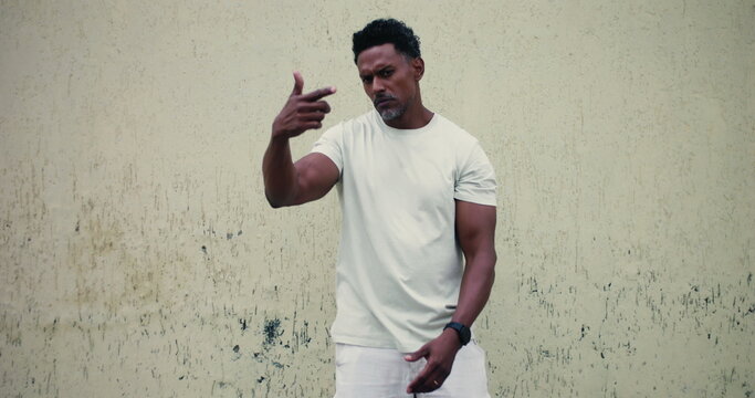 Man of African descent standing against textured wall, pointing forward with serious expression, confident and assertive body language, confrontational stance, strong presence