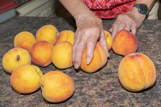 Elderly woman's hand reaching for a fresh, ripe, peach on a kitchen counter.  Senior's making healthy eating choices concept.