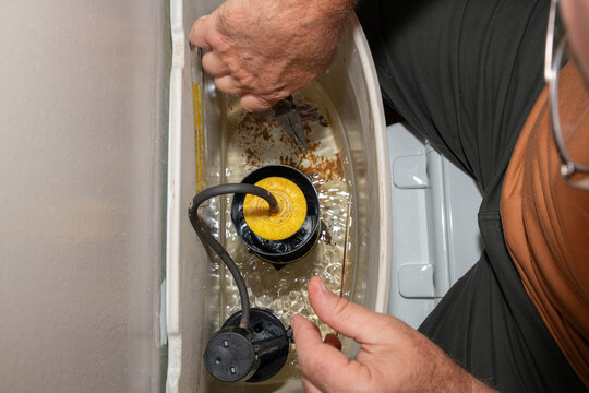 From above, repair person or homeowner working on the components of a toilet tank.