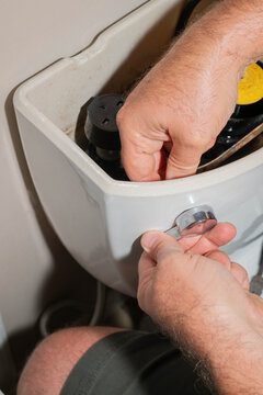 Close-up of hands removing a broken toilet flush handle.