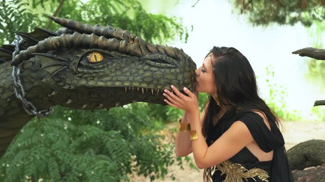 Portrait art Fantasy woman kissing dragon head. Dark queen girl touching with love mythical ancient pet animal muzzle. Summer forest green trees foliage. Lady fairy elf Black elegant romantic dress 4k