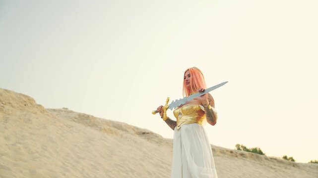 Fantasy woman warrior creative costume sexy girl goddess strong face. golden armor costume dress. Lady elf holding sword sharp blade with hands, magic weapon. Fashion model posing. sand Dune desert.