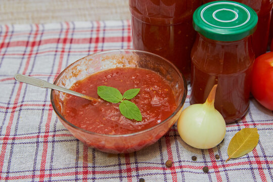 Homemade tomato sauce in a glass bowl, Homemade tomato sauce in a glass bowl with onions and spices on it and jars nearby