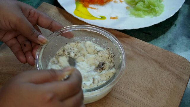 Yoghurt or curd raita, Cucumber raita in glass bowl mixing garnish overhead close up hands-only spoon lifting action.