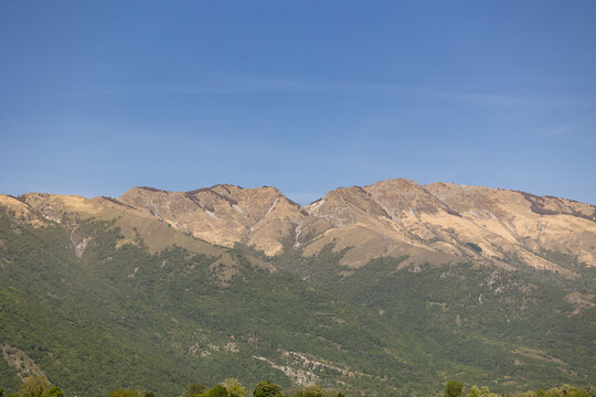 catena montuosa brulla e rocciosa con pendii inferiori coperti da fitta vegetazione boschiva sotto un cielo azzurro terso, prealpi in zona Piancavallo e Aviano, regione Friuli Venezia Giulia, Italia