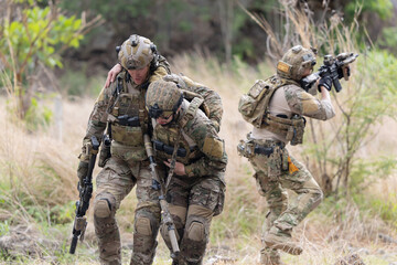 Fototapeta premium Soldier carries injured comrade over rocky terrain