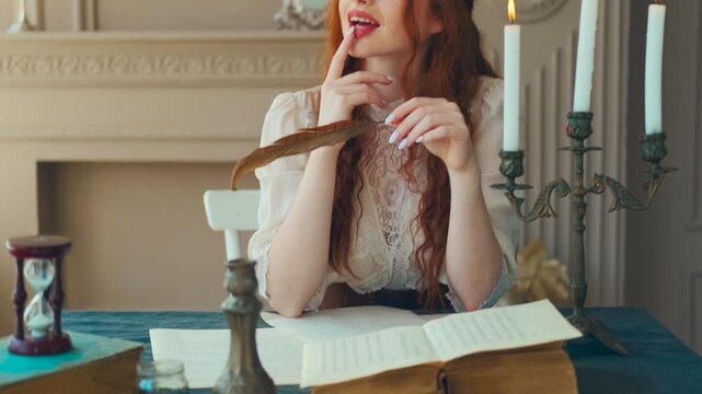 Portrait red-haired vintage woman writer holding bird feather in hands. Medieval girl sit at table writes book, letters on sheets paper with ink pen. Photo old retro style. White blouse, classic room.