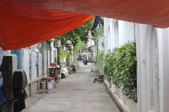 Narrow concrete alleyway in vietnam with colorful orange tarp and green plants.