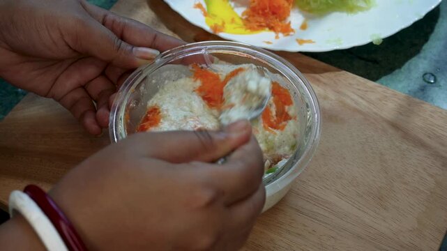 Yoghurt or curd raita, Cucumber raita in glass bowl mixing garnish overhead close up hands-only spoon lifting action.
