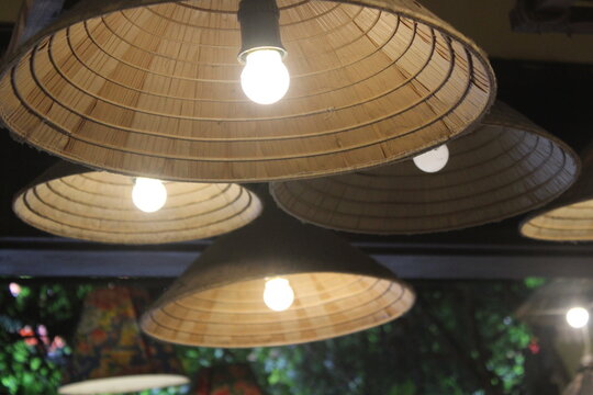 Traditional straw hat lampshades hanging from ceiling in rustic outdoor setting.