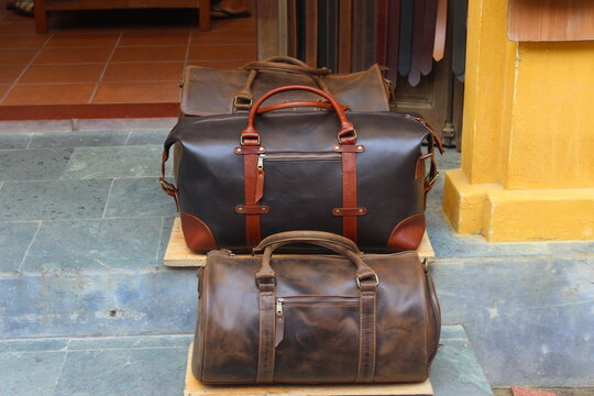 Professional leather travel bags on wooden stand outside leather shop in Vietnam.
