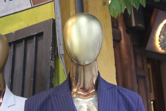 Close up portrait of golden mannequin head wearing blue pinstripe formal suit coat.
