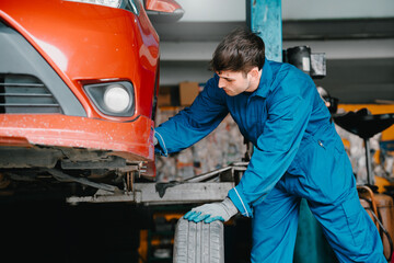 Fototapeta premium Auto repair service concept. Mechanic working near lifted red car with tire in garage for vehicle maintenance, wheel inspection, and safety care.
