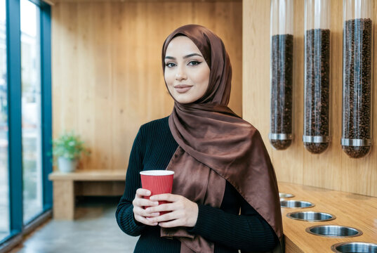 Muslim woman wearing hijab holding coffee cup in cafe