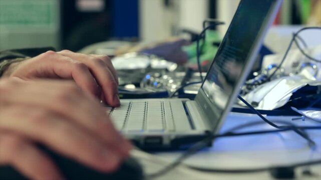 mani di giovane uomo adulto e tecnico informatico mentre  lavora ad un progetto e scrive al computer su un bancone pieno di oggetti