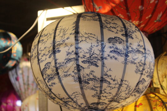 Round white silk lantern with dark blue pine tree prints hanging in gift boutique.