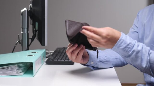 Person holding and showing an empty wallet at a desk, illustrating personal financial difficulties, budget issues, poverty, or lack of money after salary payment