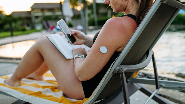 Woman looking at data in diabetes app on smartphone, wearing CGM sensor on arm.