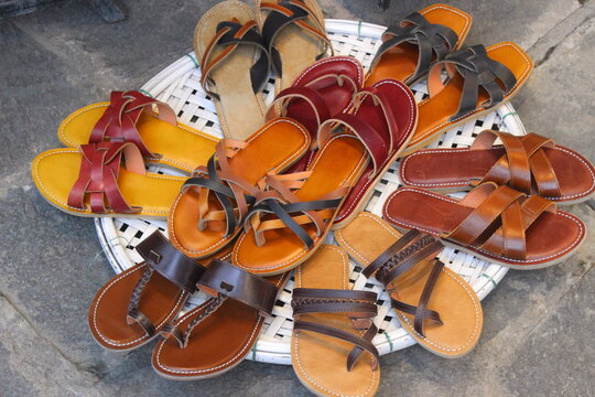 Assorted styles of woven and leather sandals arranged on white wicker basket tray.