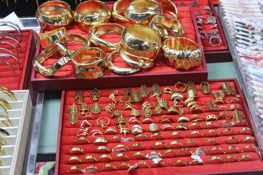 Selection of golden bracelets and rings displayed for sale on velvet tray shelves.