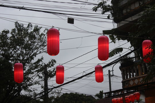 Vibrant red tube shaped lanterns suspended over urban street during overcast weather.