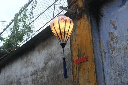 Traditional patterned lantern hanging on a yellow wall with red direction marker.
