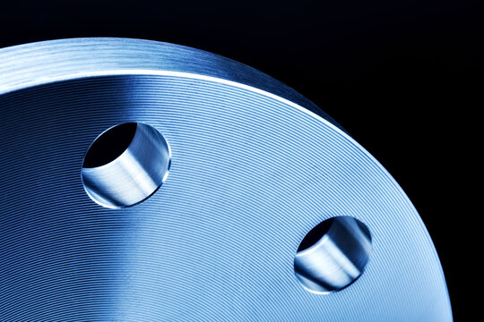 Macro close-up detail of stainless steel 304 flange with dramatic light and shadow effect, highlighting machined surfaces, concentric rings, and bolt holes.