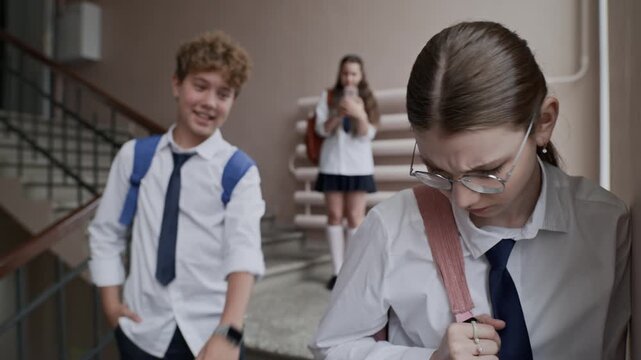 Caucasian teenage girl looking sad while Caucasian teenage boy mocking and bullying her in school hallway. Perfect for anti-bullying campaigns and mental health awareness videos