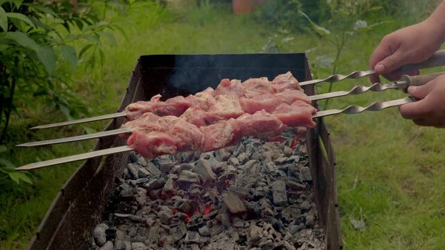The camera pans across the rows of metal skewers. Raw meat slowly changes color during the cooking process. Sparks fly from the charcoal grill in slow motion.