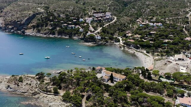 Aerial view of Platja Sa Conca, a secluded Costa Brava beach surrounded by pine-covered cliffs, elegant hillside villas and the crystal-clear waters of the Mediterranean Sea. 