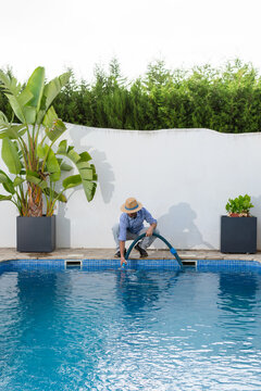 Vertical shot of pool maintenance worker inserting vacuum hose into swimming pool