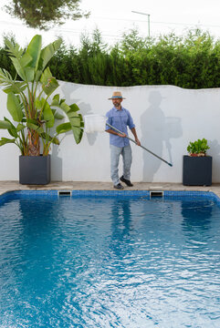 Vertical pool maintenance worker lifting skimmer net filled with debris from swimming pool