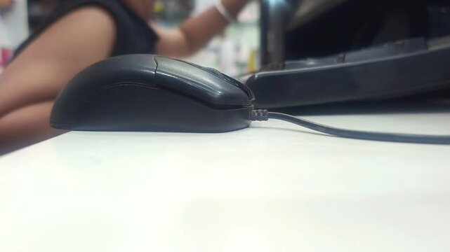 Side view of a computer mouse on a white desk with a child working in the blurred background