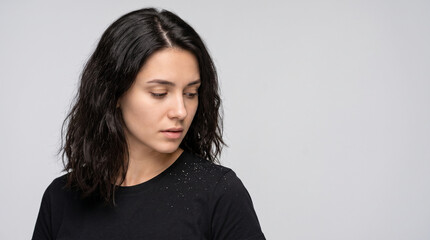 Fototapeta premium Sad Young Woman Looking at Dandruff Flakes on Black T Shirt Against Grey Background