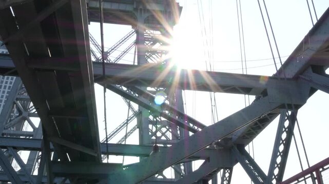 Williamsburg Bridge from Manhattan to Brooklyn, New York City, USA. Architecture of United States, tourist landmark. Metallic cable-stayed bridge. Sun rays and sky from pedestrian path. Low angle.