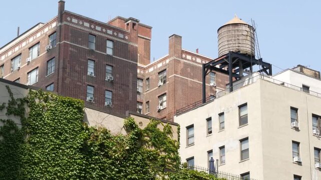 New York City urban building architecture, Manhattan rooftop, United States of America. Water tower on roof. Classic water tank. Ivy greenery on wall. Vine climber creeper plant on house, green leaves