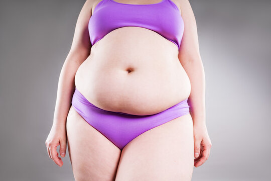Overweight woman with belly fat in underwear on gray background. Obesity, weight loss, diet and body positivity concept